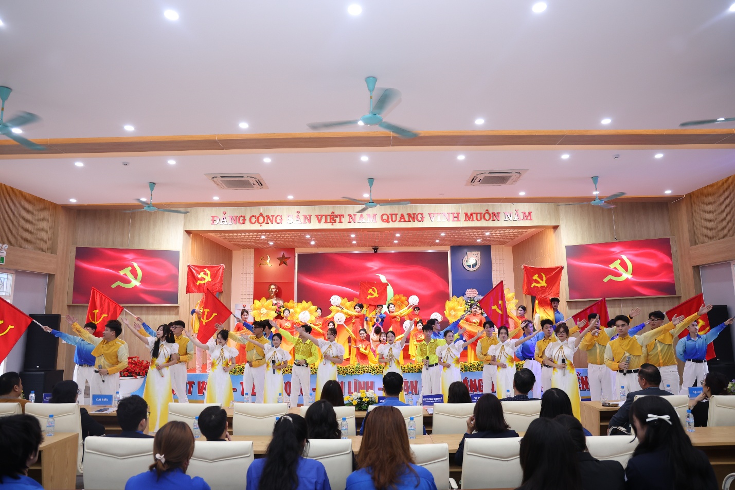 A group of people performing in a room with flags Description automatically generated