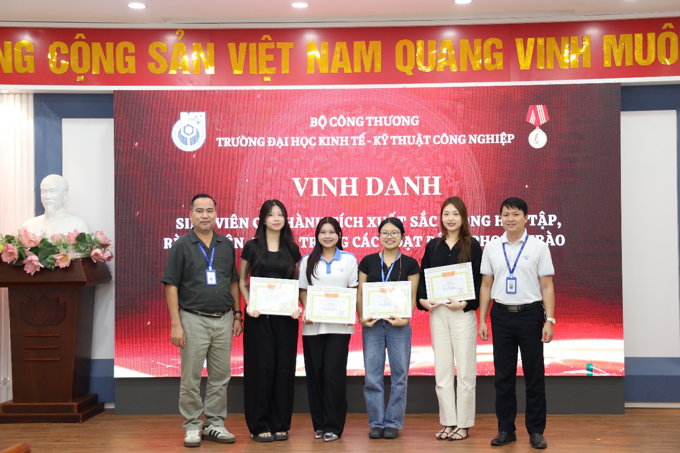 A group of people standing in front of a red banner Description automatically generated
