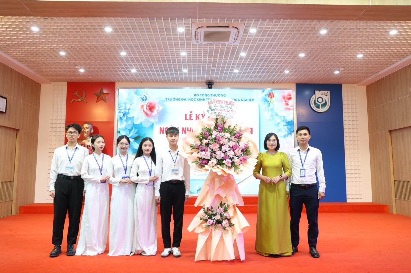 A group of people standing in a room with a person holding a bouquet of flowers Description automatically generated