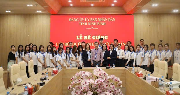 A group of people standing in front of a red wall Description automatically generated