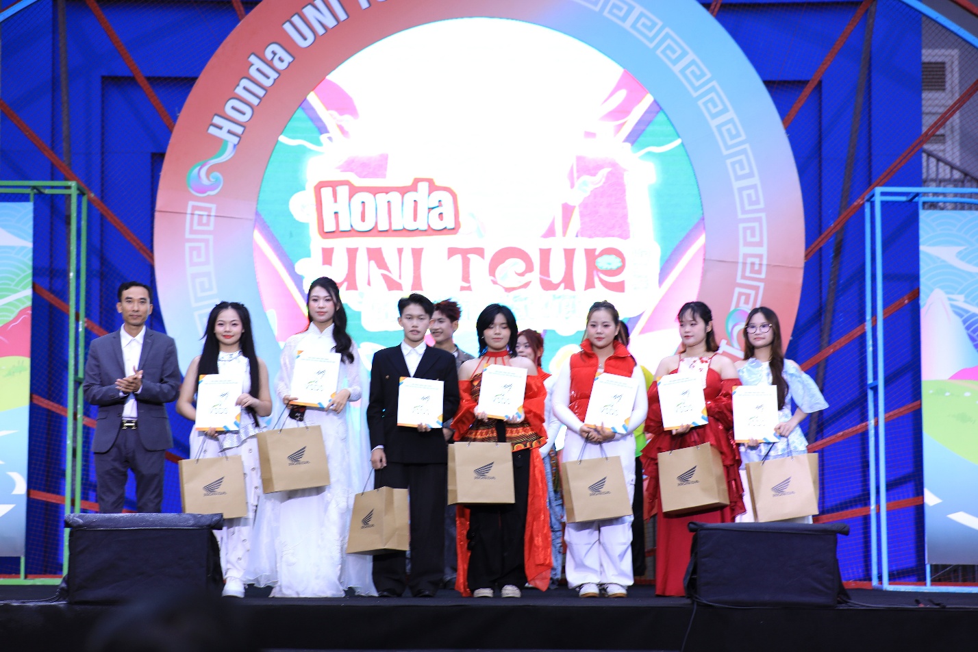 A group of people on a stage holding bags Description automatically generated
