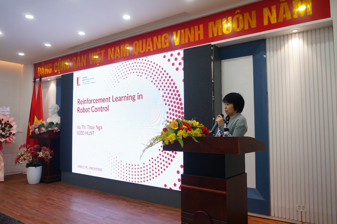 A person standing at a podium with a large screen Description automatically generated