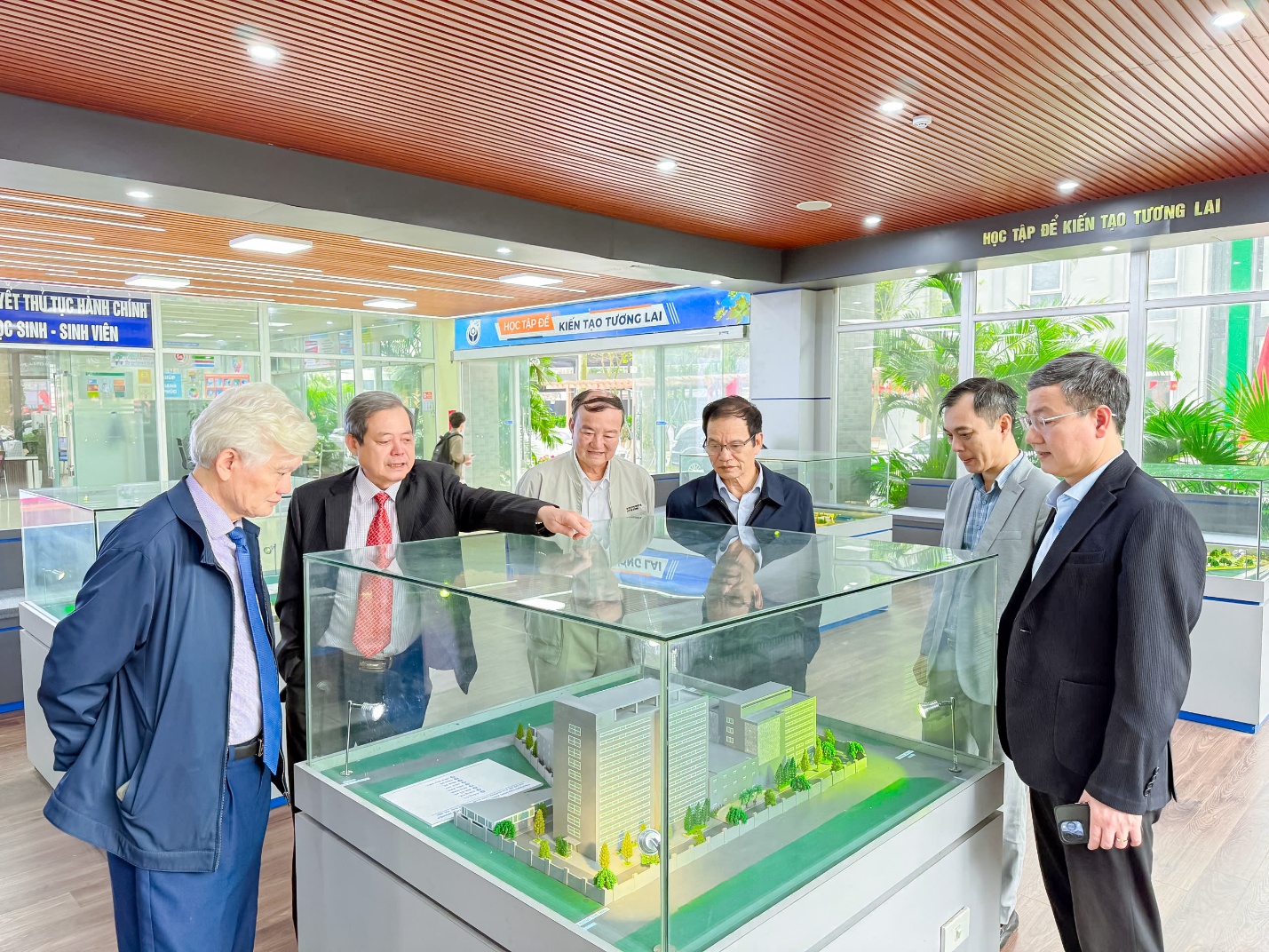 A group of men in suits looking at a model Description automatically generated