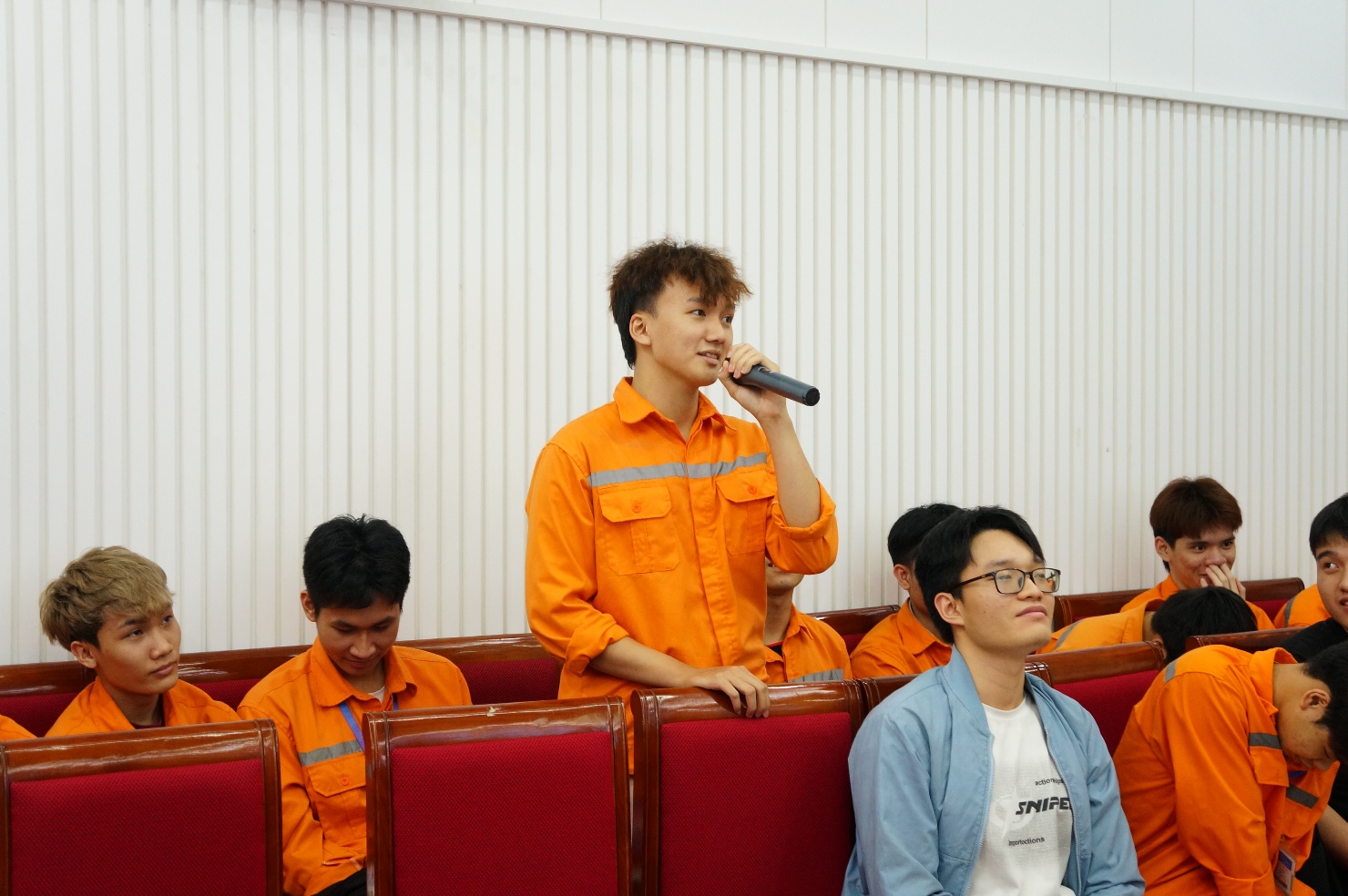 A person in an orange jumpsuit speaking into a microphone
Description automatically generated
