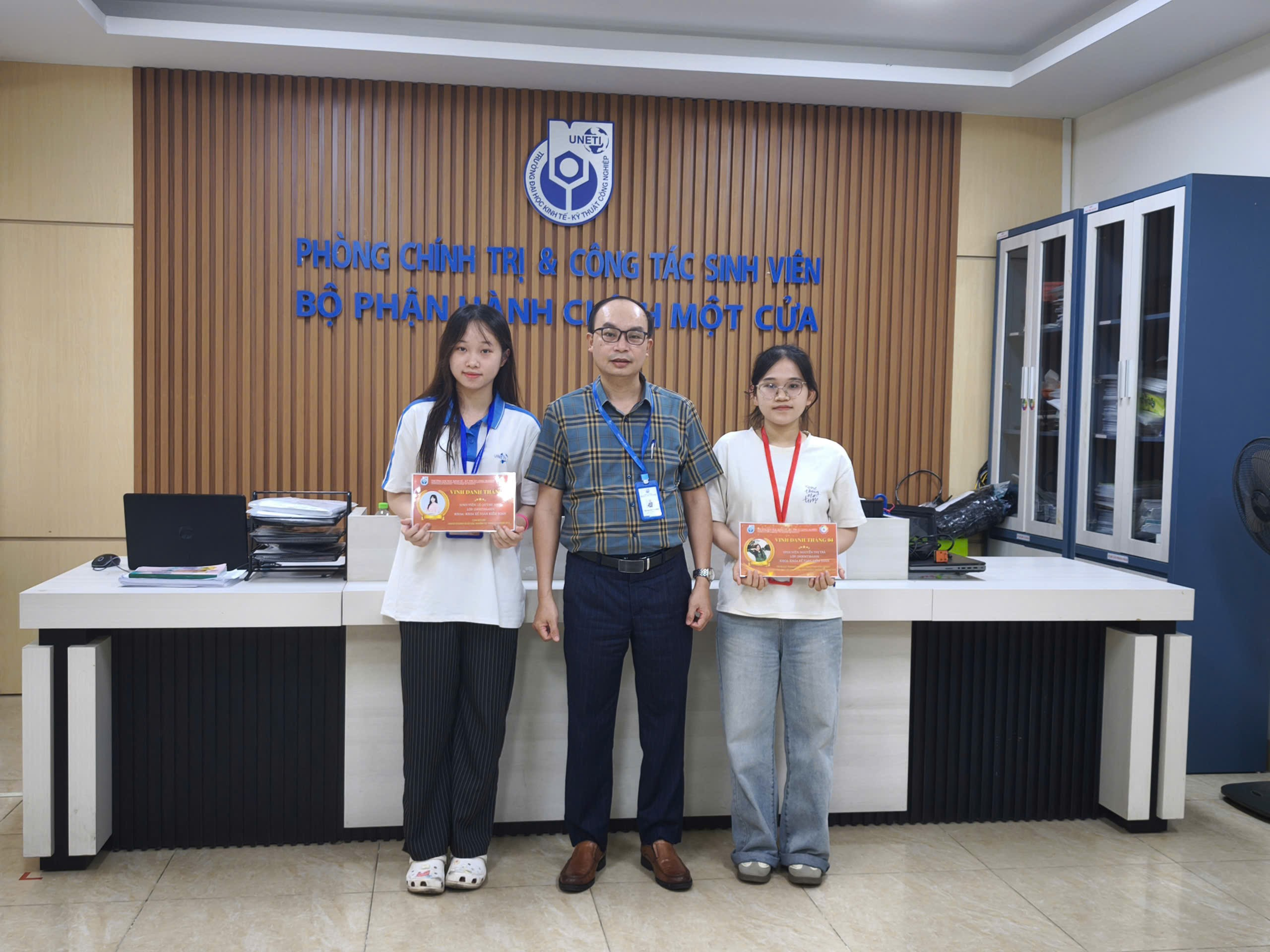A group of people standing in front of a desk Description automatically generated