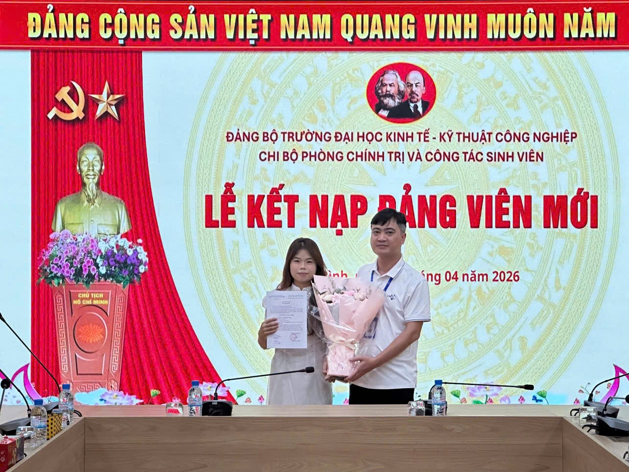 A person and person standing at a podium holding a couple of paper
Description automatically generated