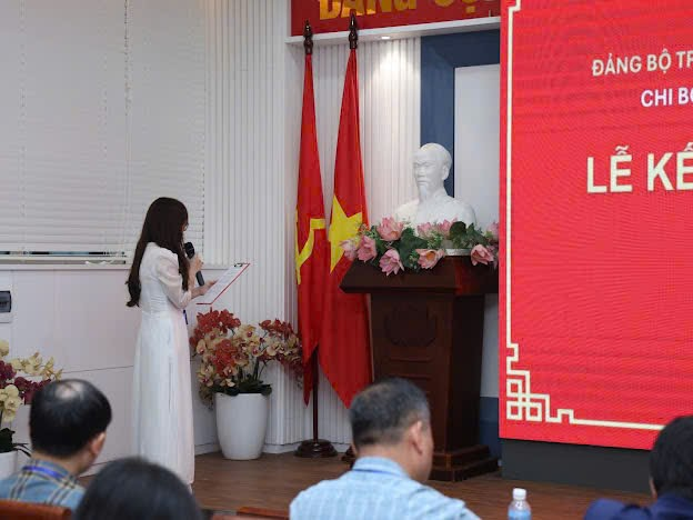 A person in a white dress standing in front of a podium with a flag and a statue of a person
Description automatically generated