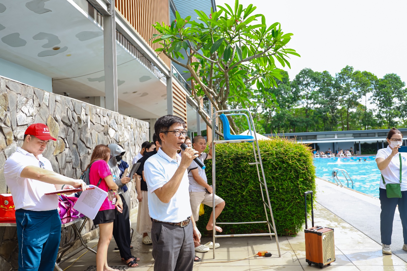 A person singing into a microphone next to a pool Description automatically generated